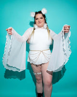 Woman in white mesh bell sleeves and playful accessories, showcasing a trendy rave outfit against a teal background.