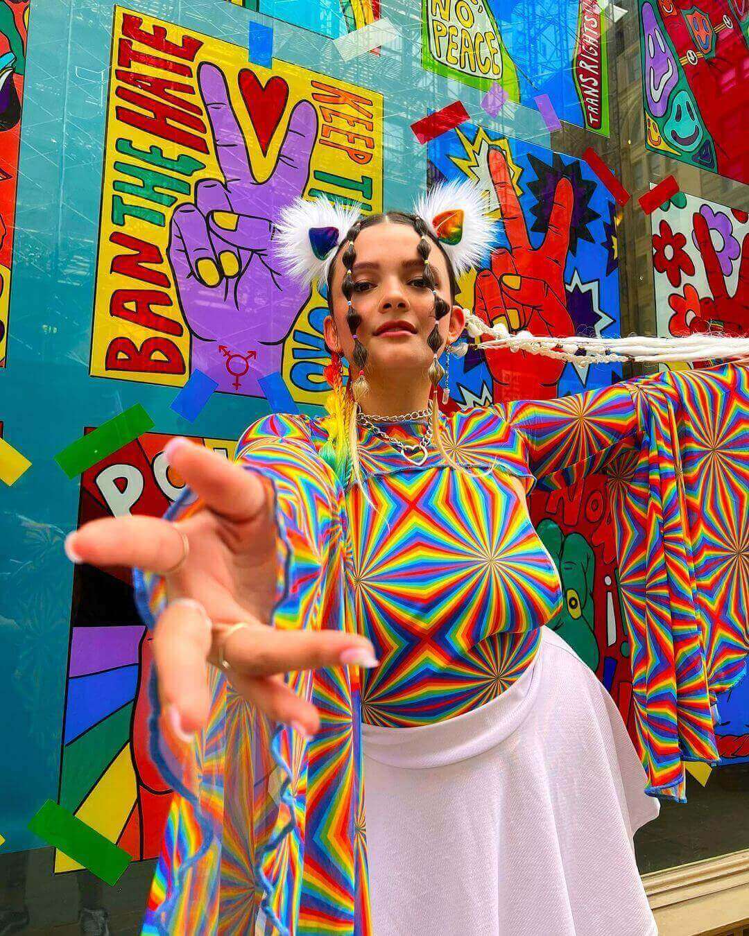 Model wearing a colorful rainbow top and white mesh skater skirt against a vibrant, graffiti-style backdrop.