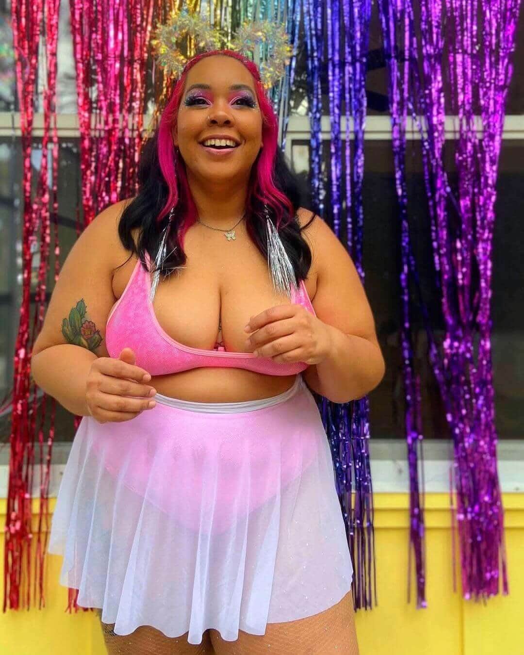 Woman wearing a pink mesh skater skirt and top, smiling joyfully in front of colorful metallic streamers.